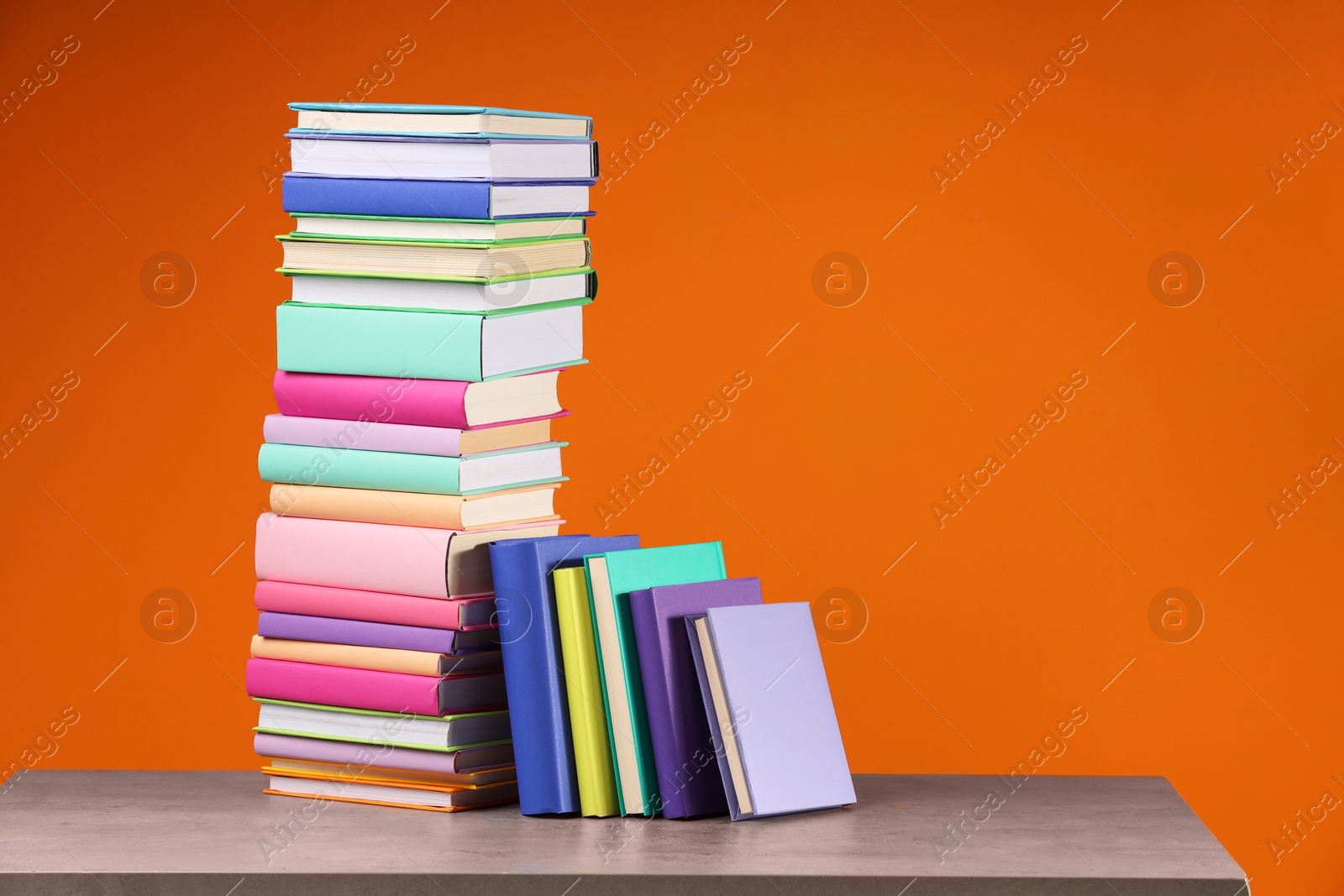 Photo of Stack of colorful books on wooden table against orange background, space for text