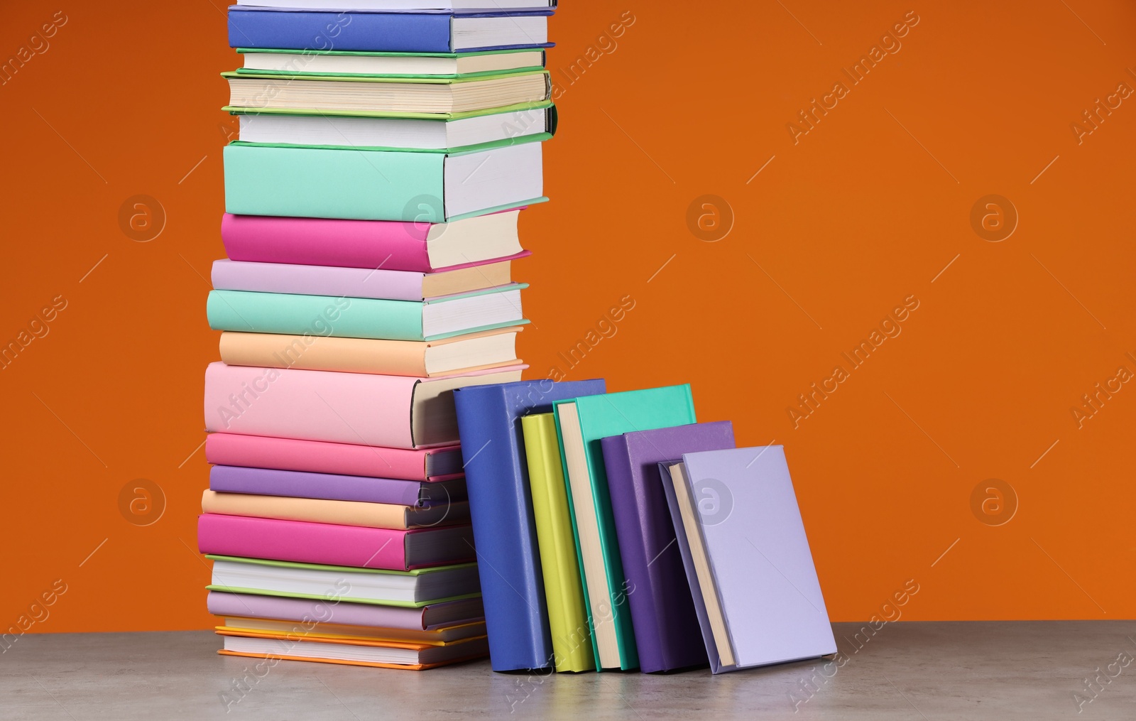 Photo of Stack of colorful books on wooden table against orange background