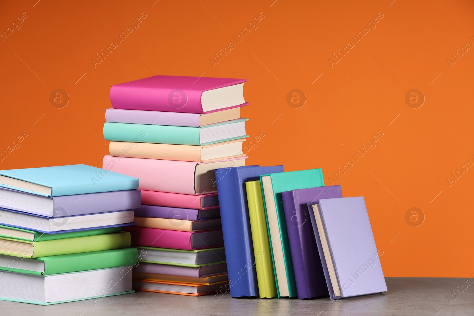 Photo of Stacks of colorful books on wooden table against orange background