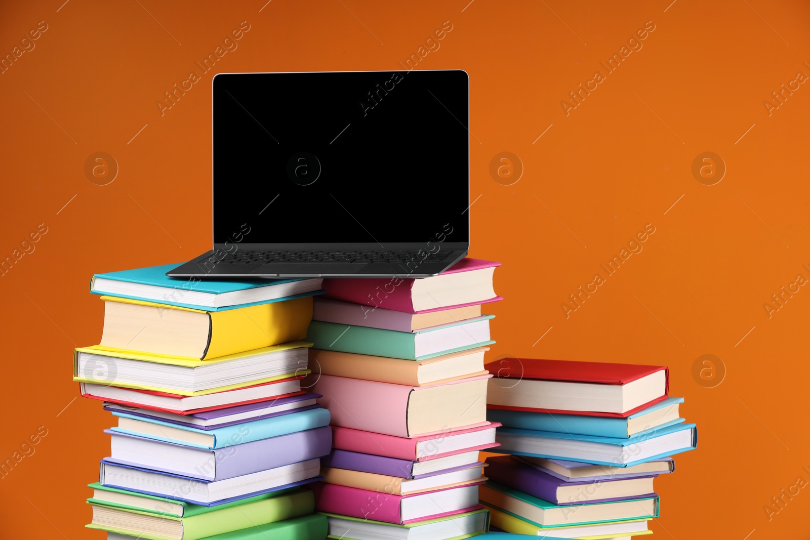 Photo of Stacks of colorful books and laptop on orange background