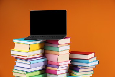 Photo of Stacks of colorful books and laptop on orange background