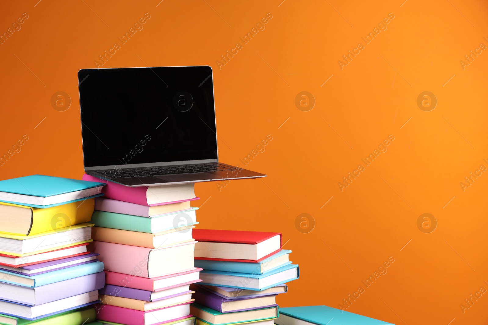 Photo of Stacks of colorful books and laptop on orange background, space for text