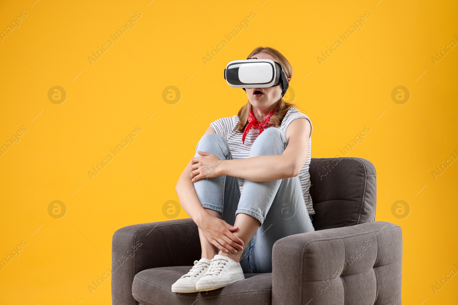 Photo of Emotional woman with virtual reality headset sitting in armchair on yellow background, space for text