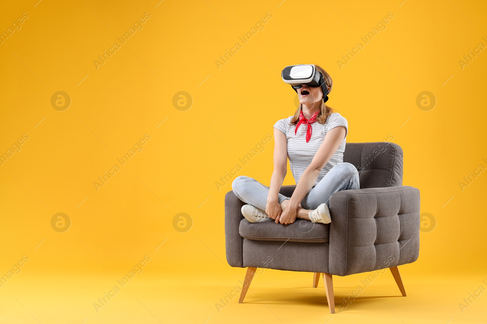 Photo of Emotional woman with virtual reality headset sitting in armchair on yellow background, space for text