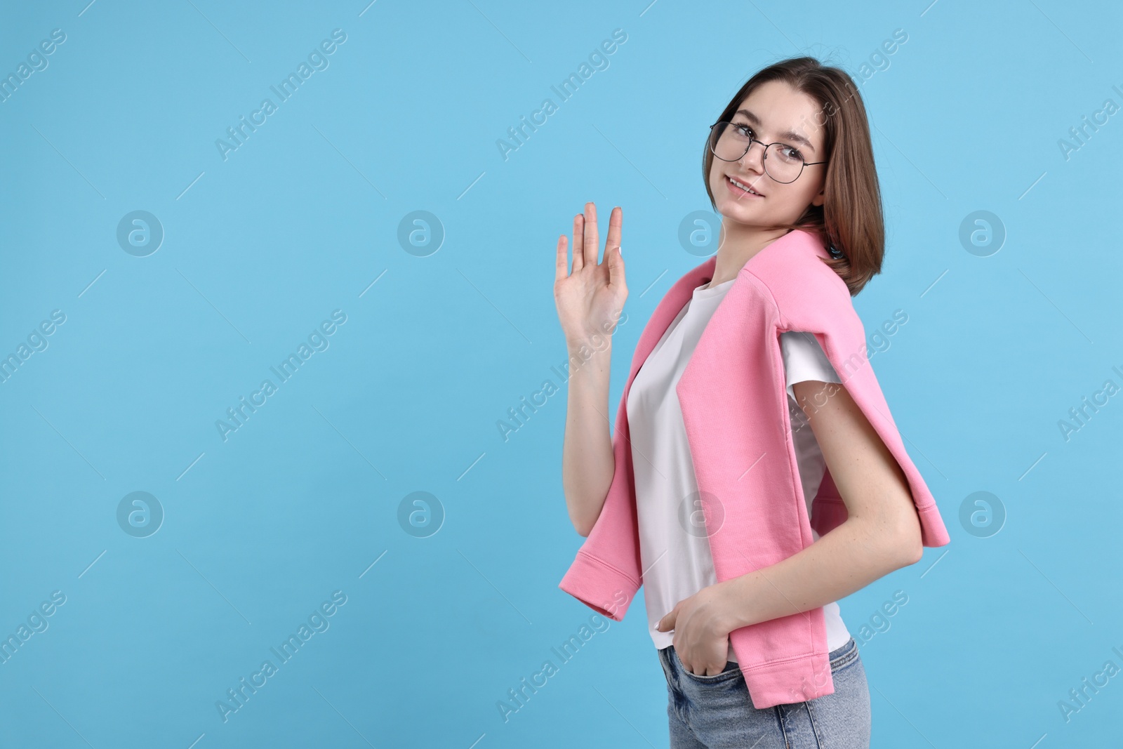 Photo of Happy teenage girl waving on light blue background, space for text