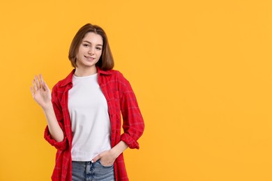 Happy teenage girl waving on orange background, space for text