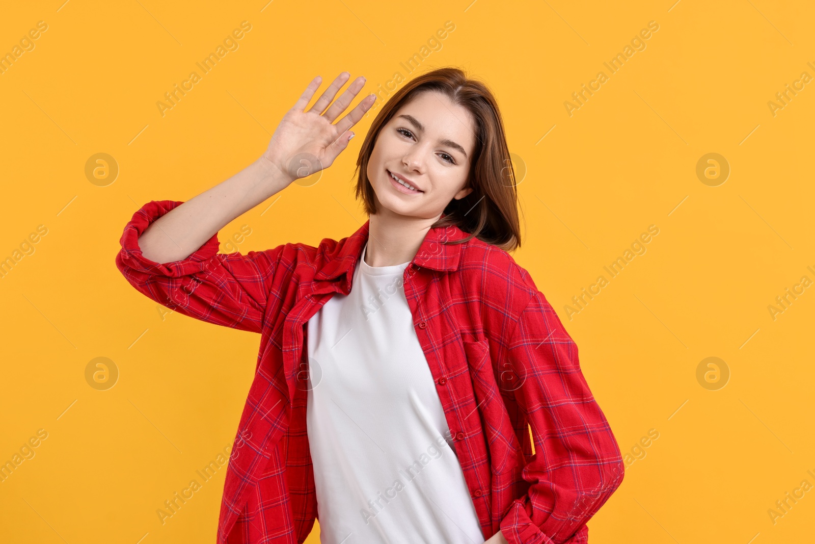 Photo of Happy teenage girl waving on orange background