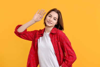 Happy teenage girl waving on orange background