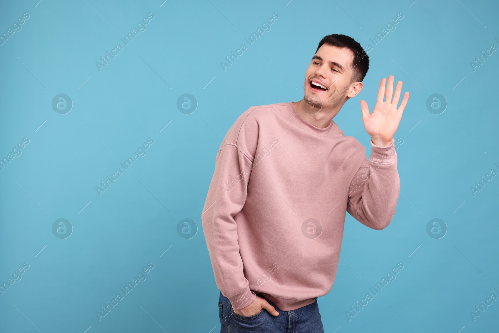 Photo of Happy young man waving on light blue background, space for text