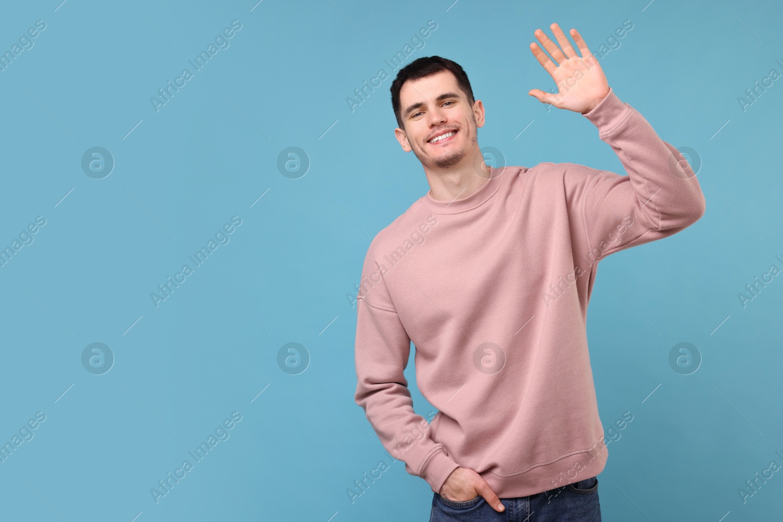 Photo of Happy young man waving on light blue background, space for text