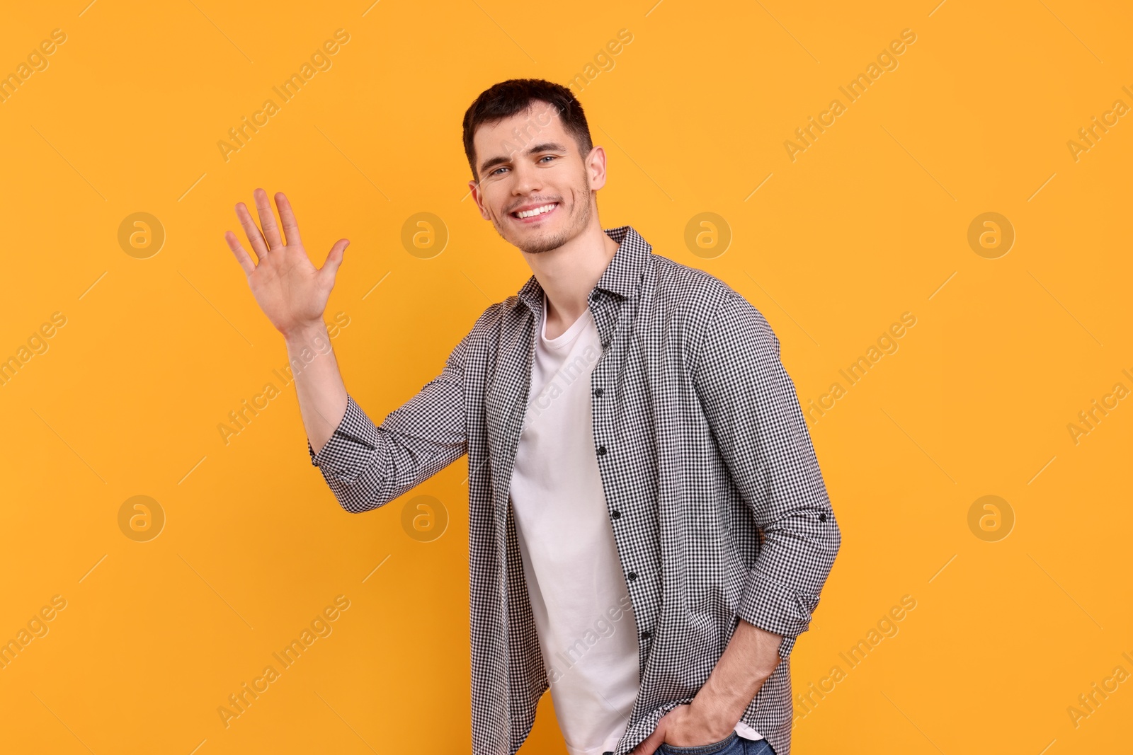 Photo of Happy young man waving on orange background