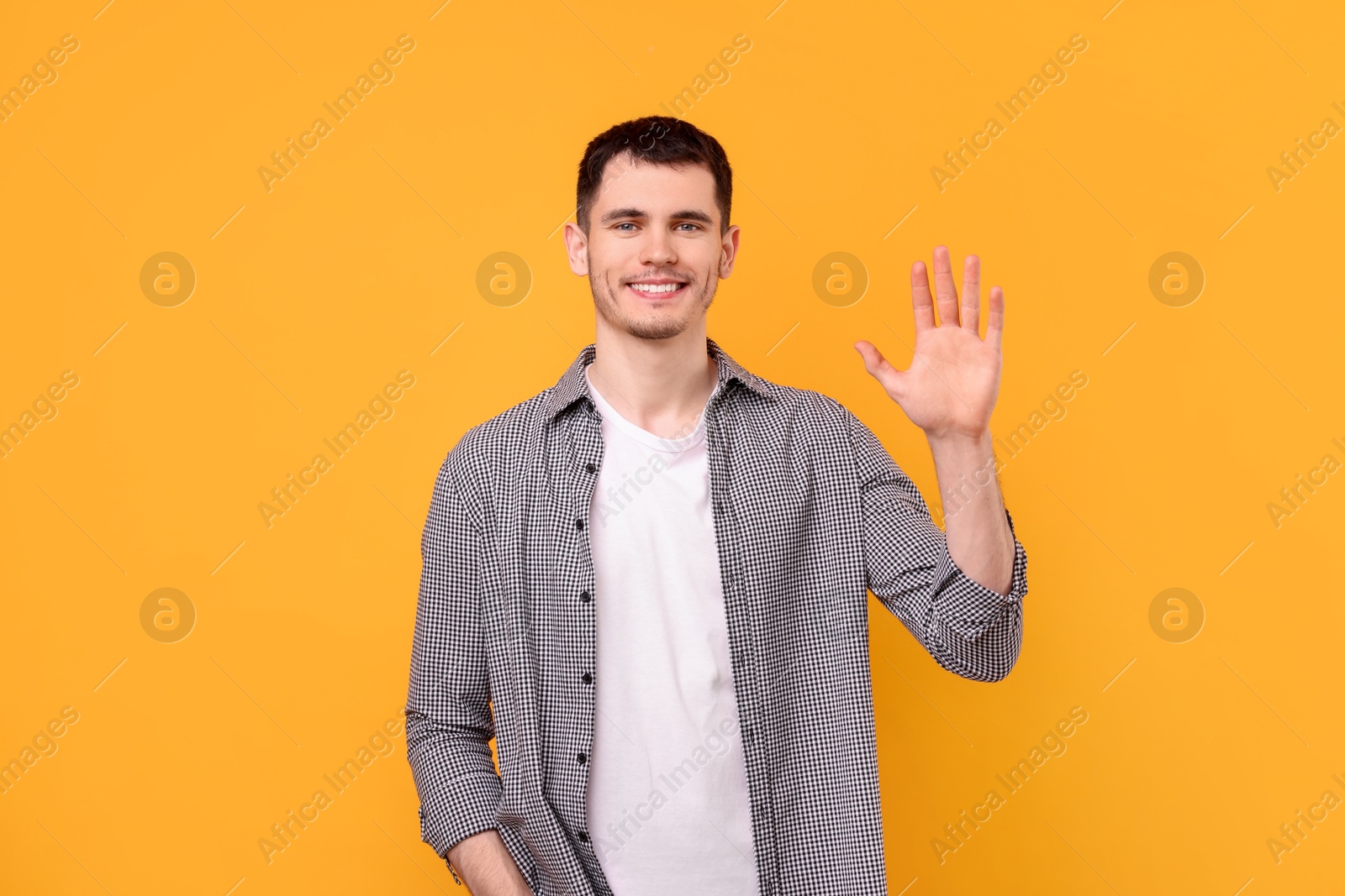 Photo of Happy young man waving on orange background