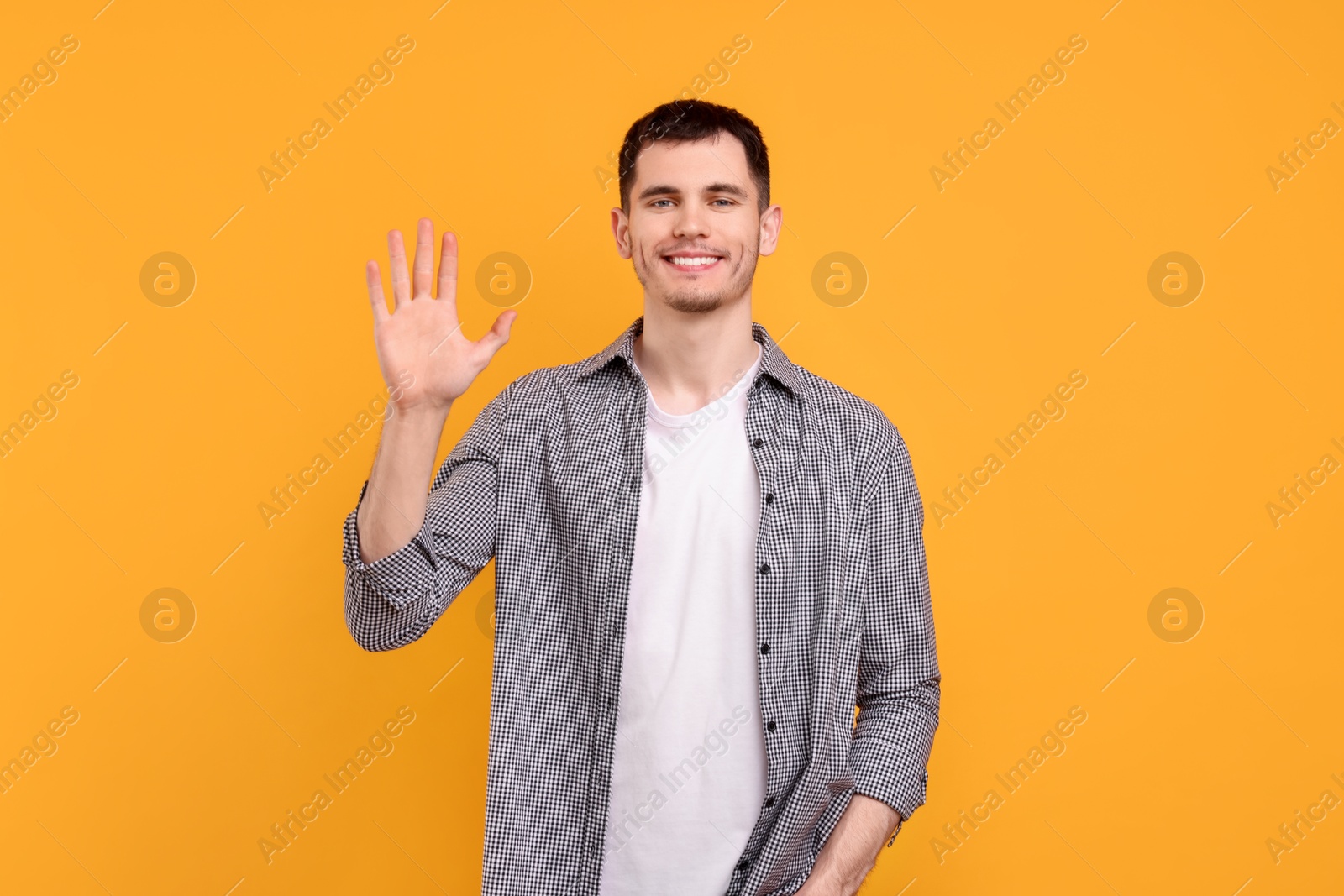 Photo of Happy young man waving on orange background