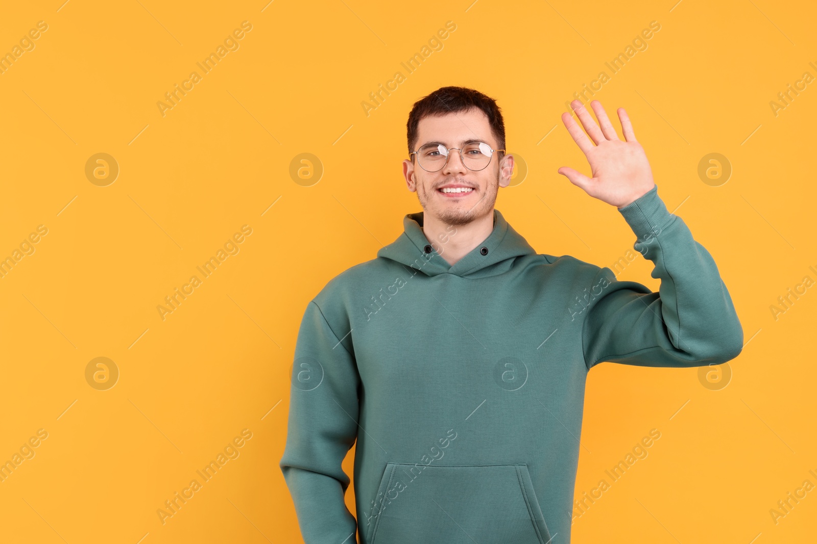 Photo of Happy young man waving on orange background, space for text