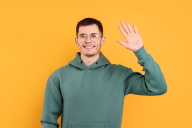 Happy young man waving on orange background