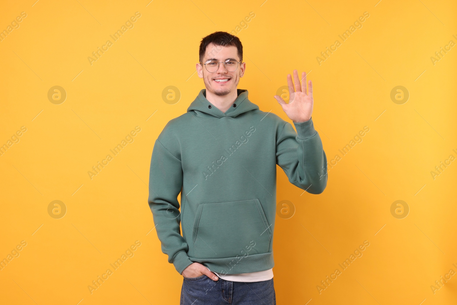 Photo of Happy young man waving on orange background