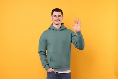 Happy young man waving on orange background