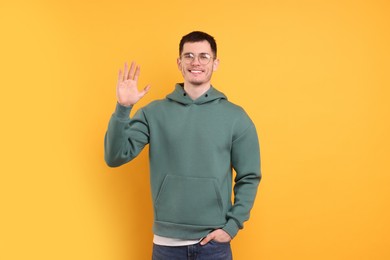 Photo of Happy young man waving on orange background