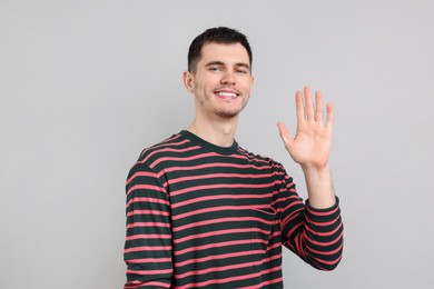 Photo of Happy young man waving on gray background