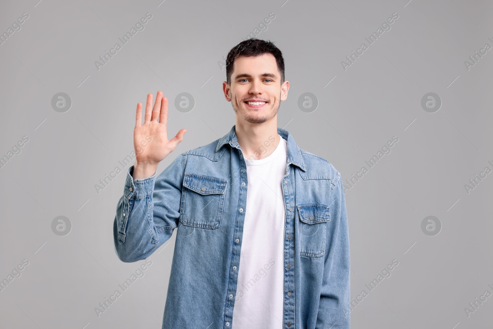 Photo of Happy young man waving on gray background