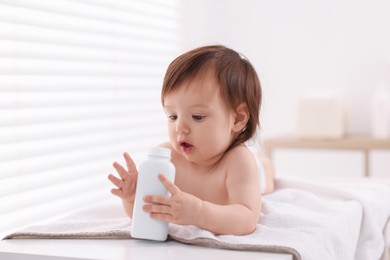 Photo of Cute little girl with bottle of dusting powder on changing table indoors