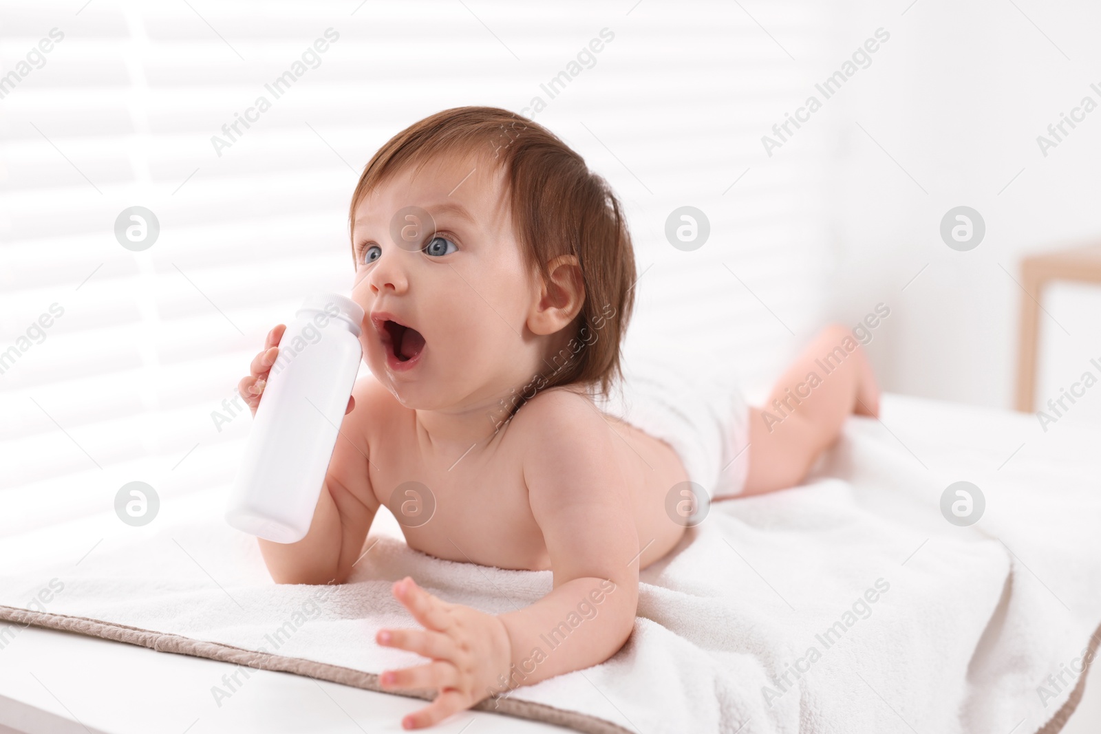 Photo of Cute little girl in diaper with bottle of dusting powder on changing table indoors