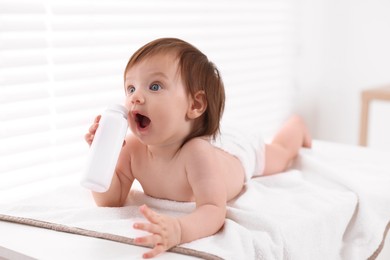 Cute little girl in diaper with bottle of dusting powder on changing table indoors