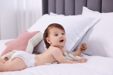 Photo of Cute little girl in diaper with wooden teether and toy bunny on bed at home