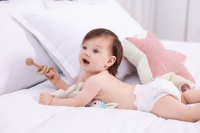 Photo of Cute little girl in diaper with wooden teether and toy bunny on bed at home