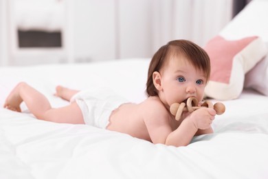 Photo of Cute little girl in diaper with wooden teether on bed at home