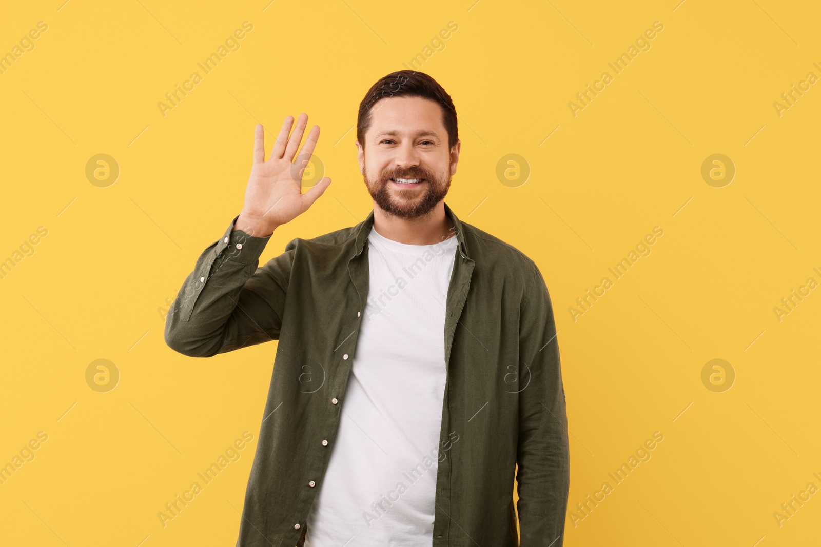 Photo of Cheerful handsome man waving on orange background