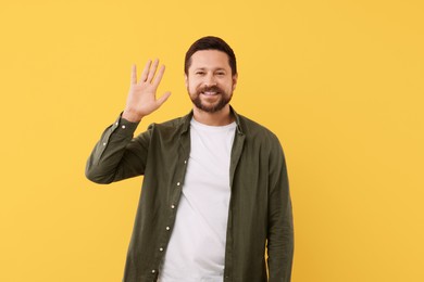 Cheerful handsome man waving on orange background