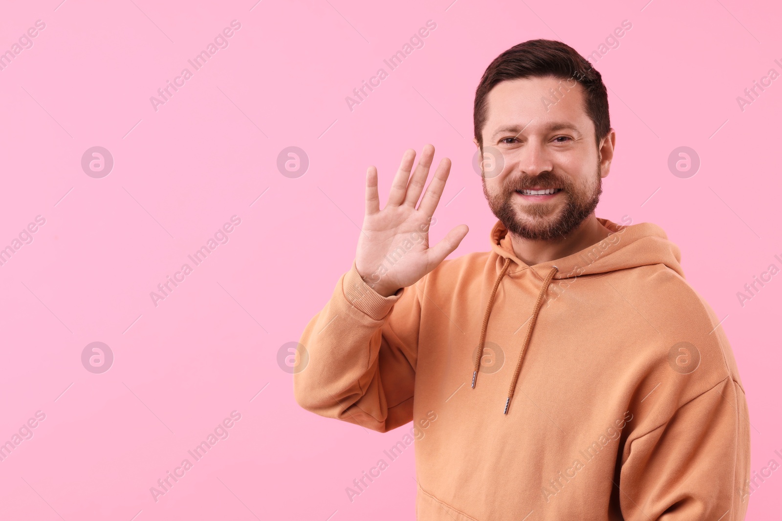 Photo of Cheerful man waving on pink background. Space for text