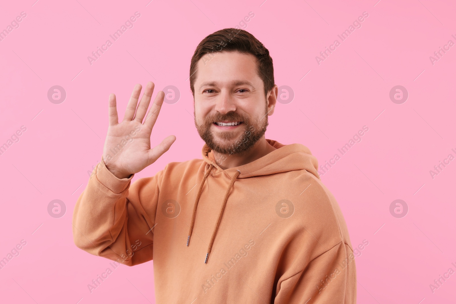 Photo of Cheerful handsome man waving on pink background