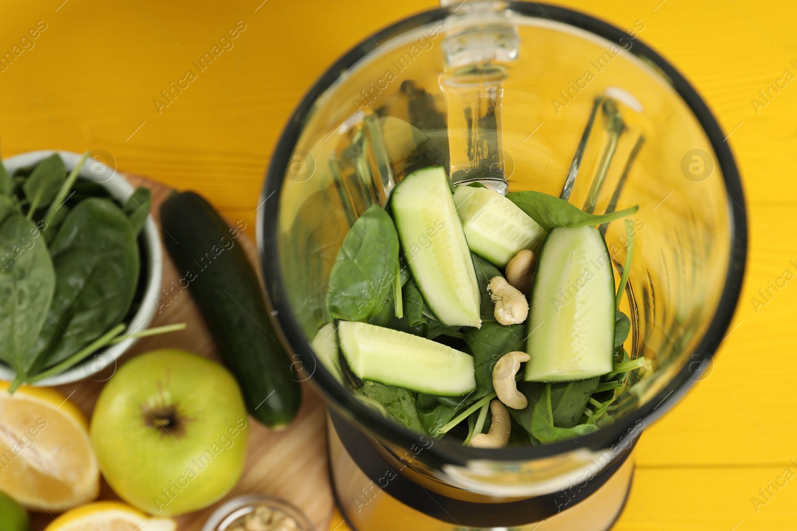 Photo of Modern blender with ingredients for smoothie on yellow wooden table, above view