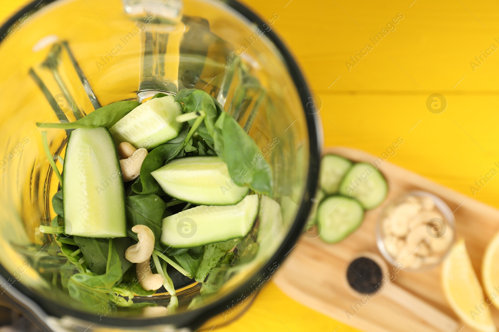 Photo of Modern blender with ingredients for smoothie on yellow wooden table, top view