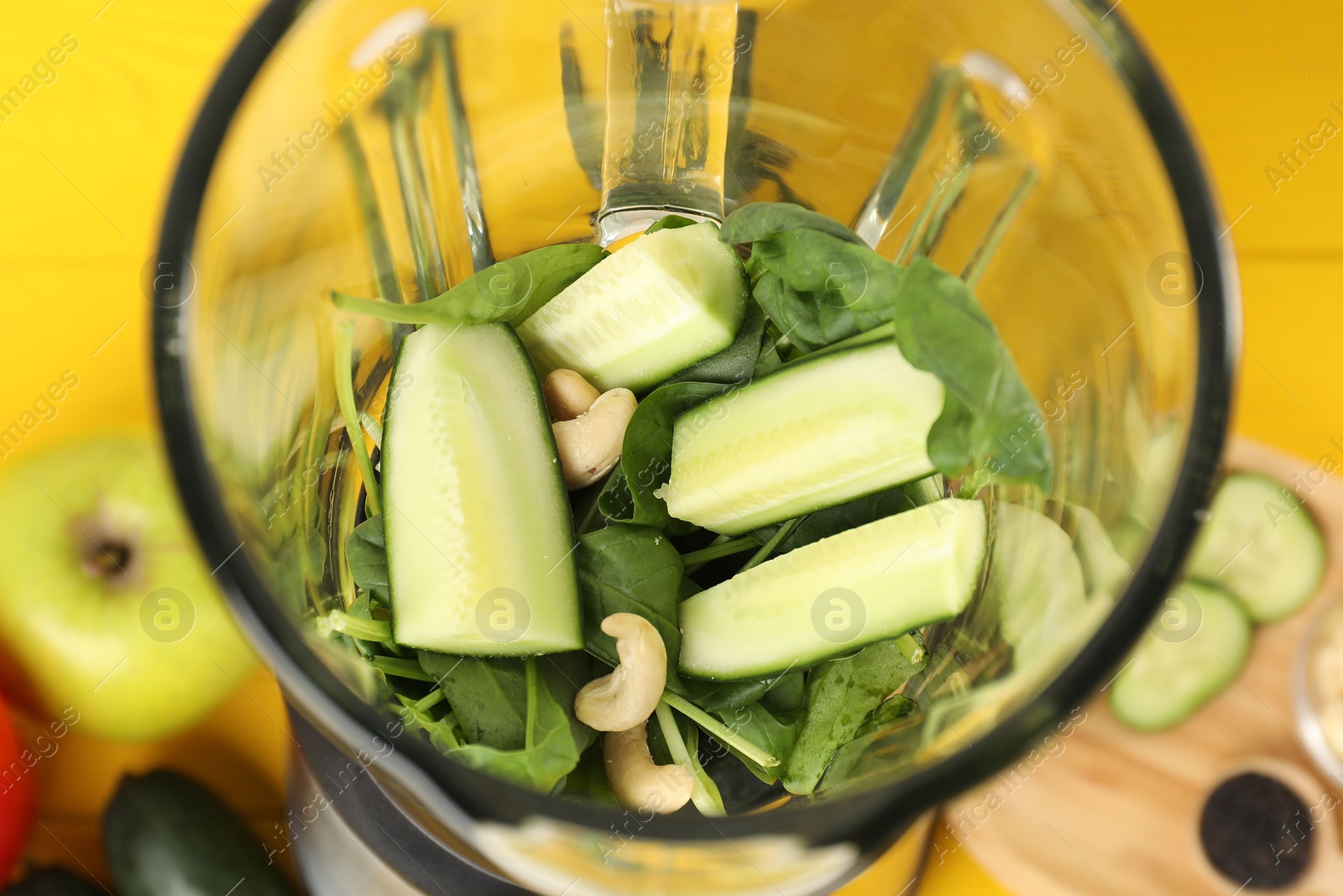 Photo of Modern blender with ingredients for smoothie on yellow wooden table, closeup