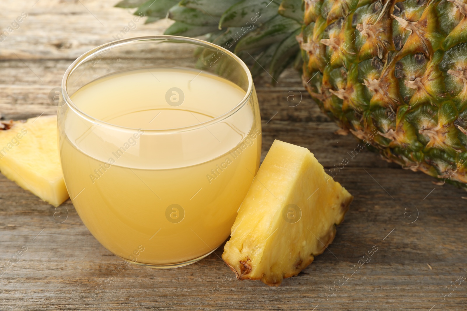 Photo of Tasty pineapple juice in glass and fresh fruit on wooden table, closeup