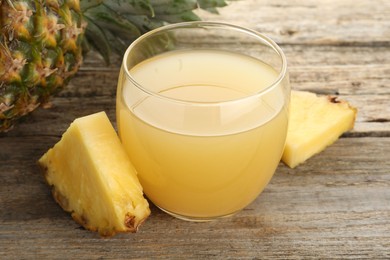 Photo of Tasty pineapple juice in glass and fresh fruit on wooden table, closeup