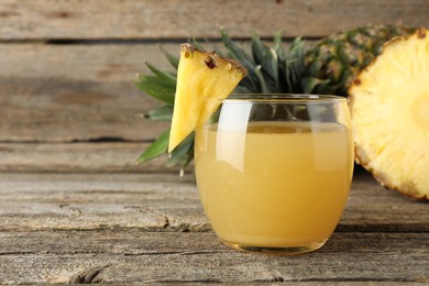 Photo of Tasty pineapple juice in glass and fresh fruit on wooden table, closeup. Space for text