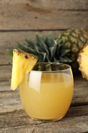 Photo of Tasty pineapple juice in glass and fresh fruit on wooden table, closeup