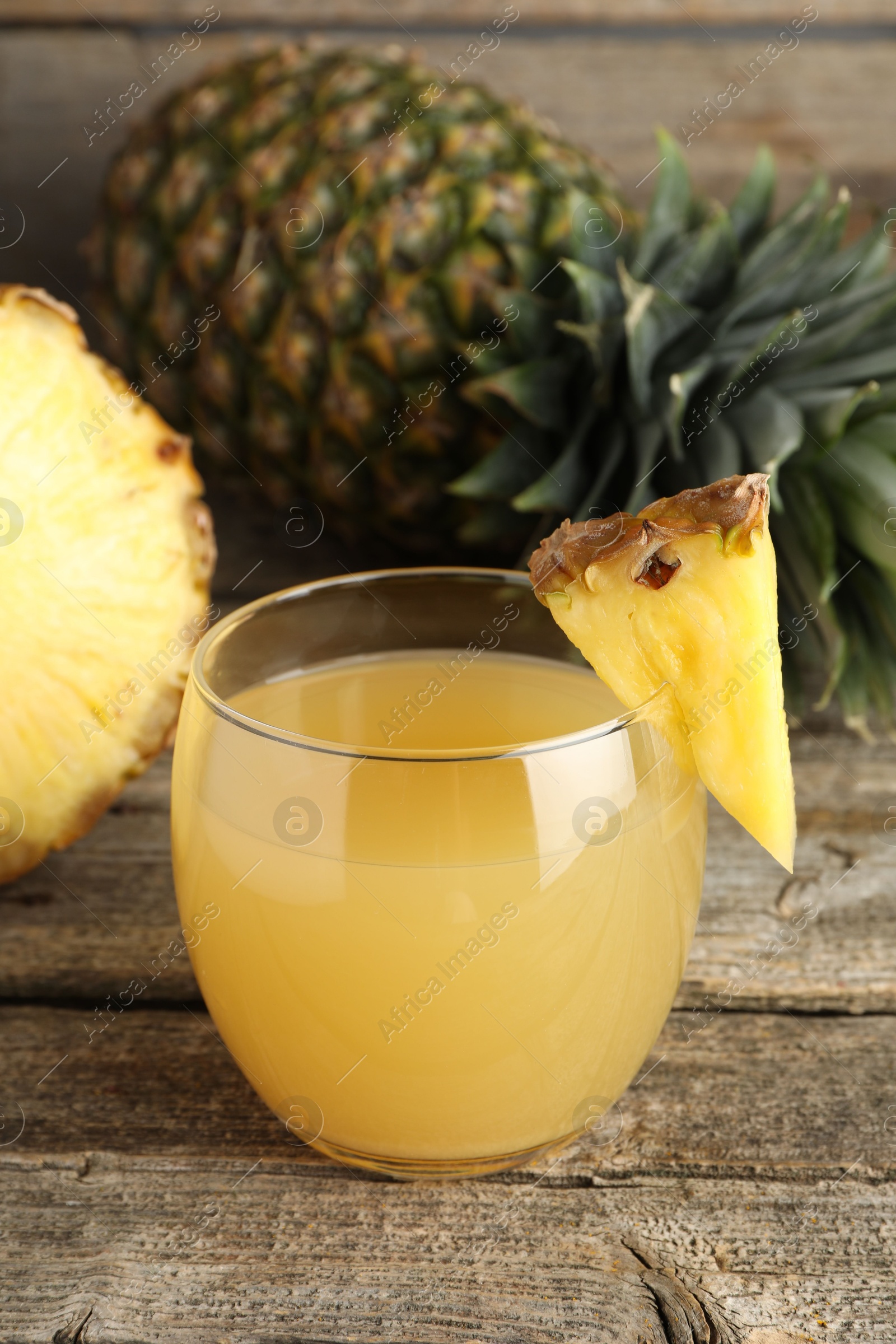 Photo of Tasty pineapple juice in glass and fresh fruit on wooden table, closeup