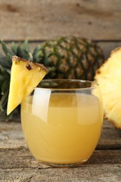 Photo of Tasty pineapple juice in glass and fresh fruit on wooden table, closeup