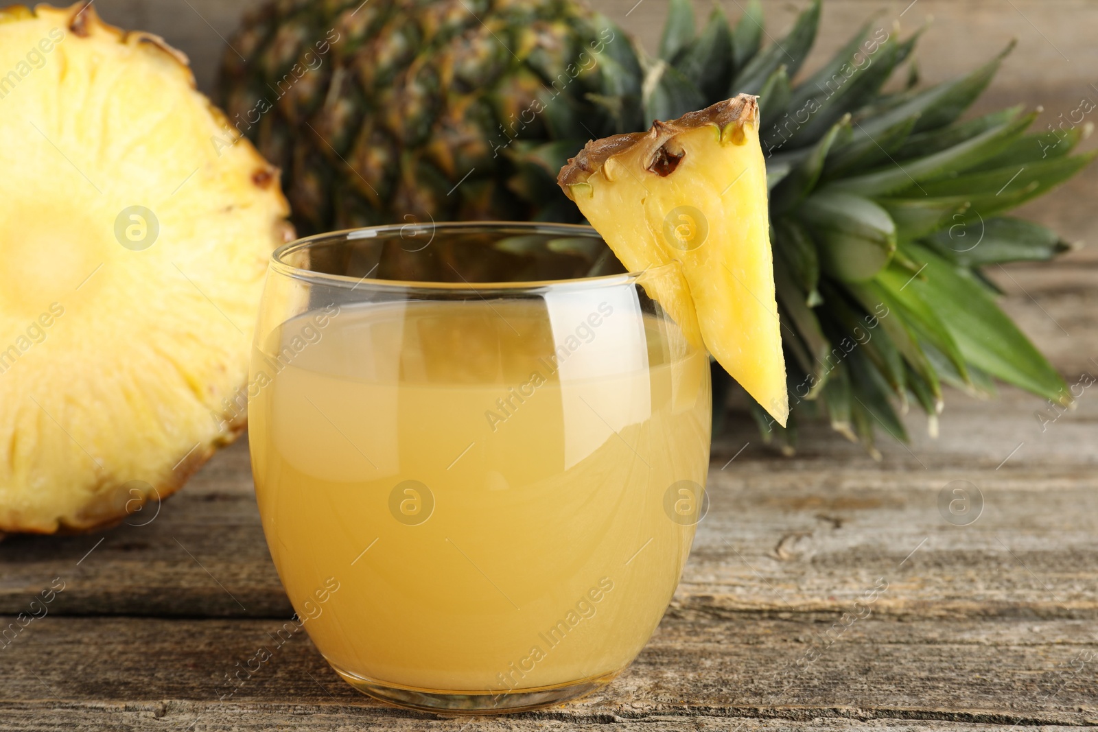 Photo of Tasty pineapple juice in glass and fresh fruit on wooden table, closeup