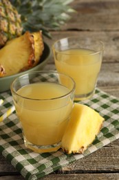 Photo of Tasty pineapple juice in glasses and slice of fresh fruit on wooden table, closeup