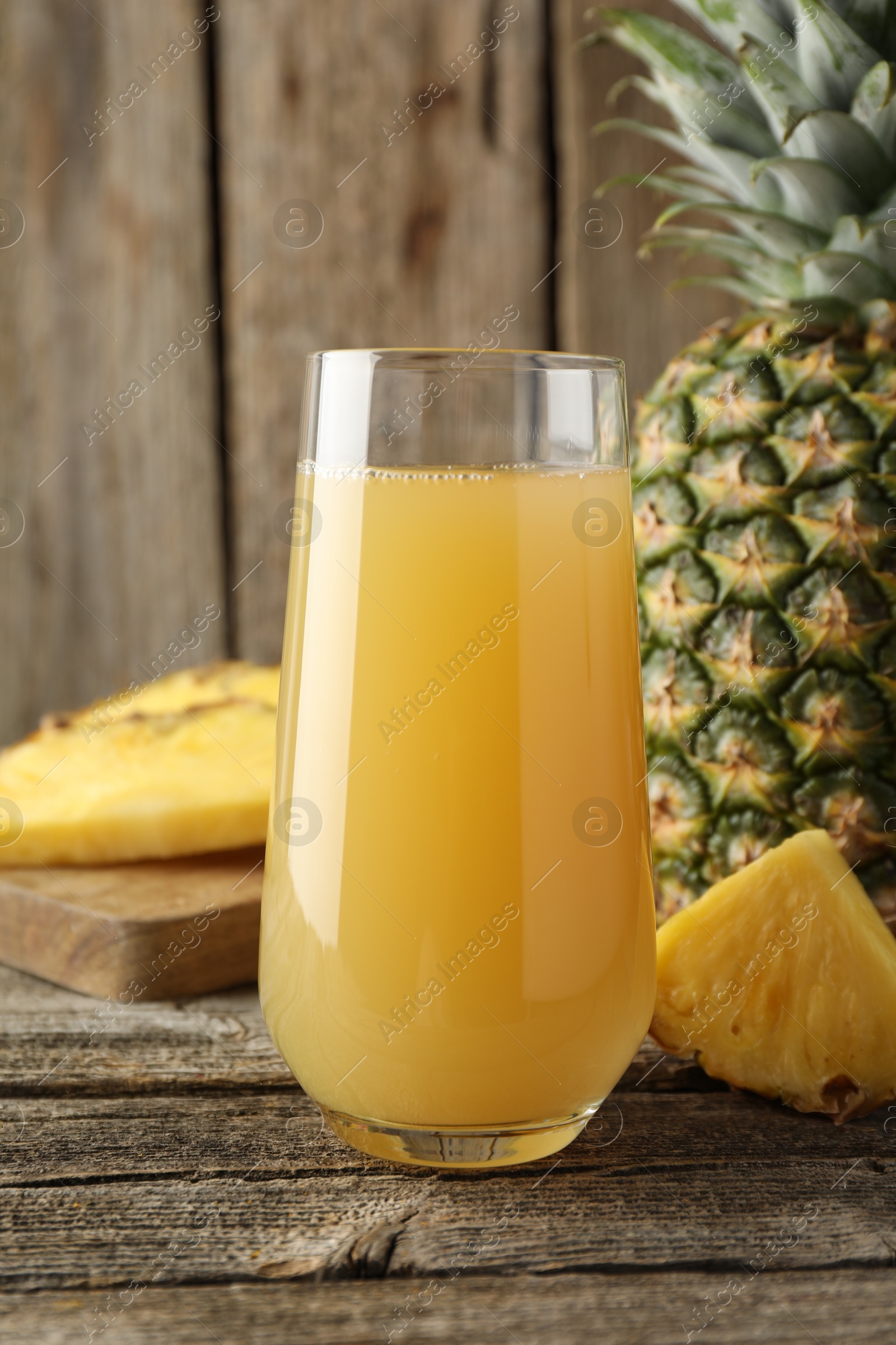 Photo of Tasty pineapple juice in glass and fresh fruit on wooden table, closeup