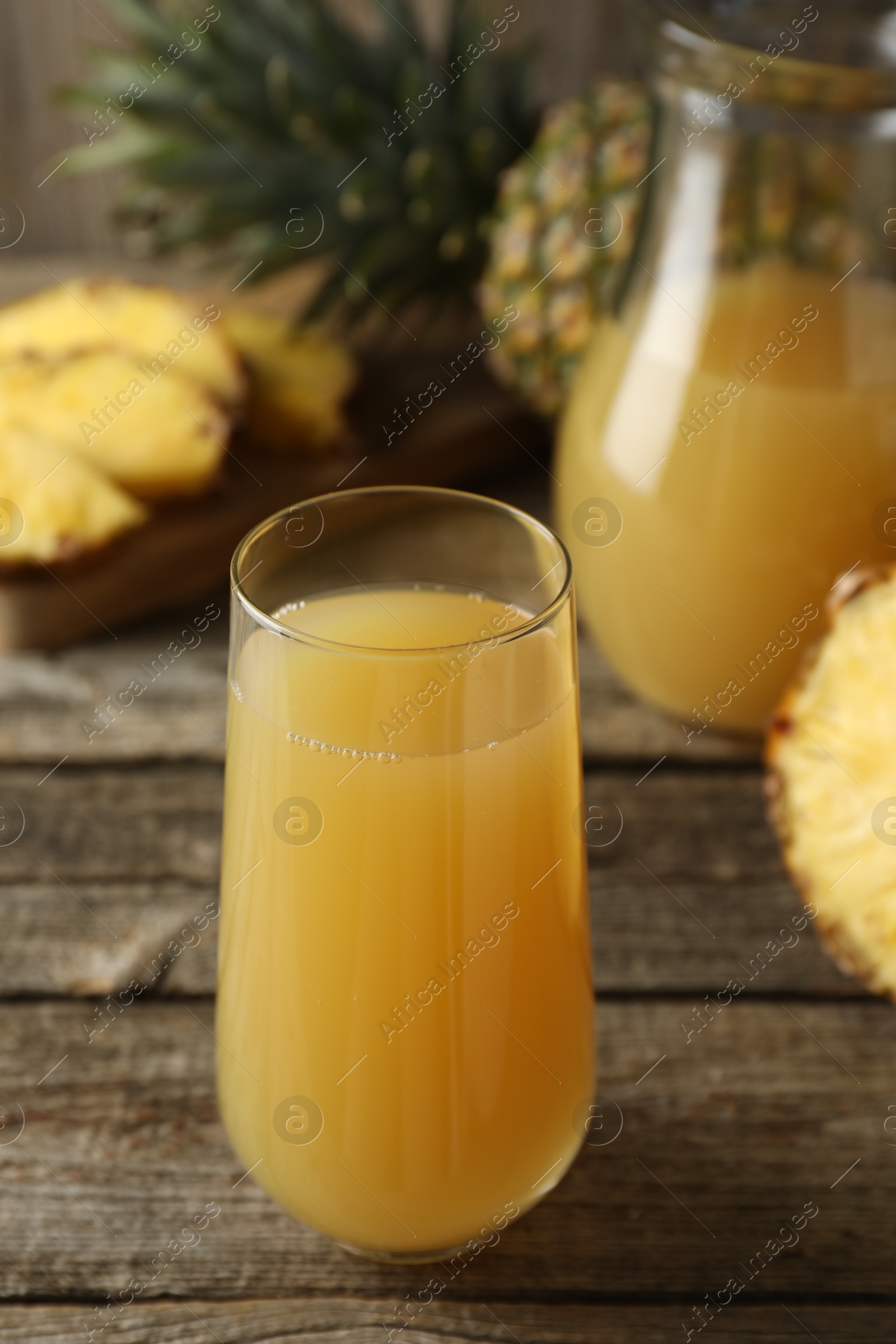 Photo of Tasty pineapple juice in glass and fresh fruit on wooden table, closeup