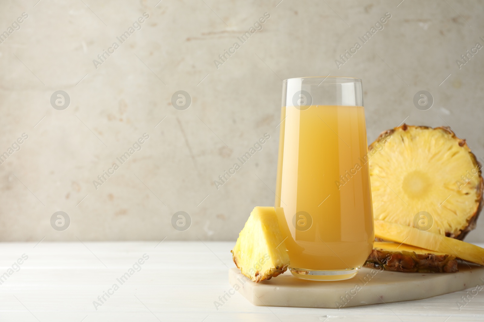 Photo of Tasty pineapple juice in glass and slices of fresh fruit on white wooden table against grey background, closeup. Space for text