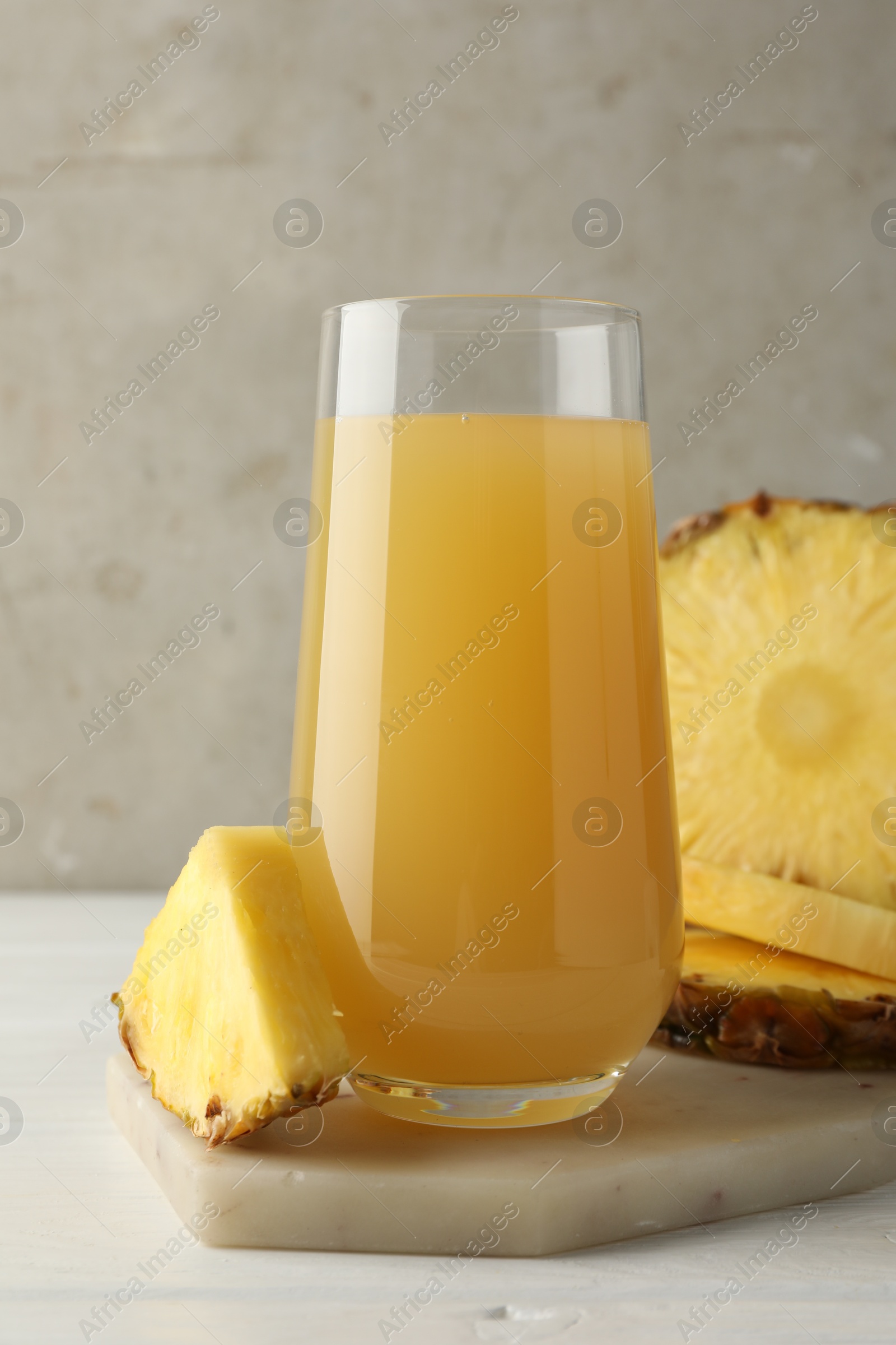 Photo of Tasty pineapple juice in glass and slices of fresh fruit on white wooden table against grey background, closeup