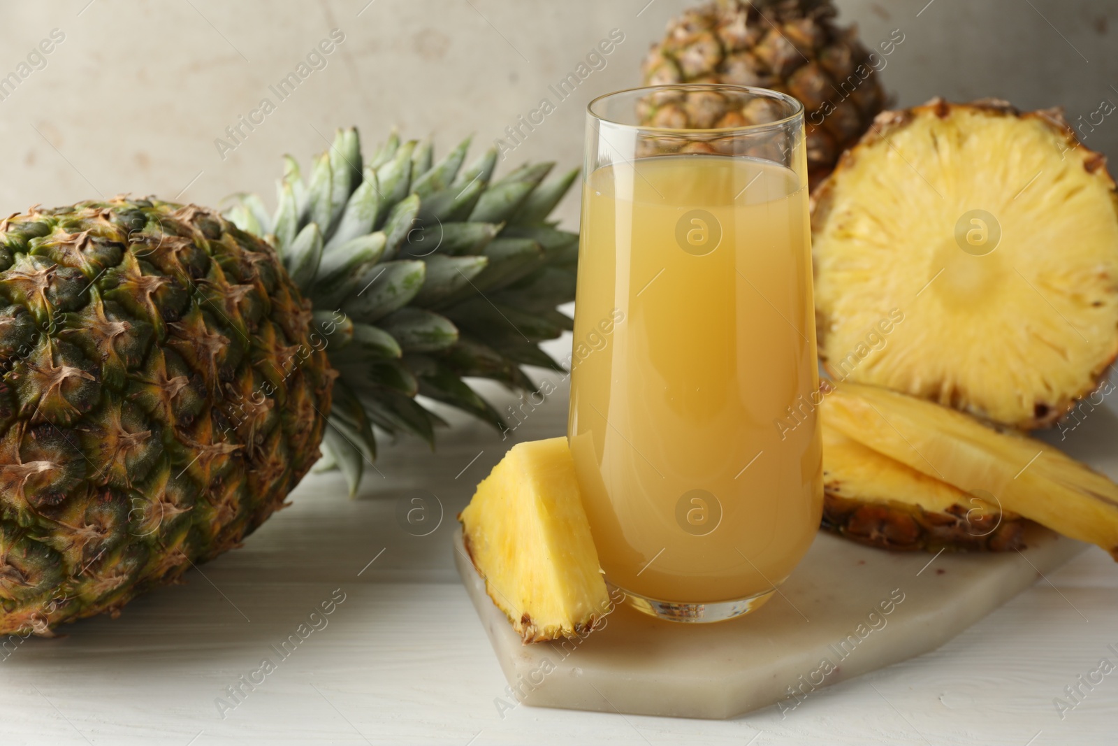 Photo of Tasty pineapple juice in glass and fresh fruits on white wooden table against grey background, closeup